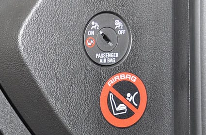 Interruptor con llave para desactivar el airbag del pasajero junto a un adhesivo que prohíbe instalar una silla infantil orientada hacia atrás con el airbag activo.